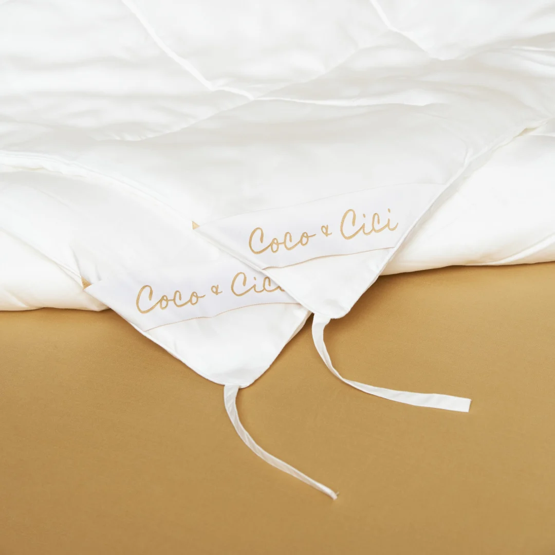 Een Dekbedovertrek 100x135 Ontspannen sfeer wit dekbed ligt op een gebruinde ondergrond, met twee witte stoffen banden die in de hoek zijn vastgemaakt.