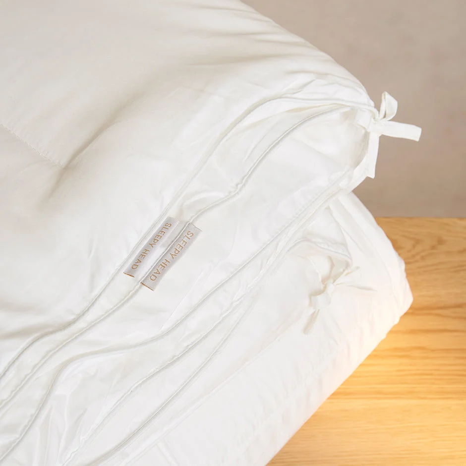 Een netjes gevouwen Dekbedovertrek 100x135 Ontspannen sfeer met zichtbare hoekbanden rust op een licht houten oppervlak. Een SLEEPERYARO label is bevestigd aan het dekbedovertrek, tegen een neutrale beige achtergrond.