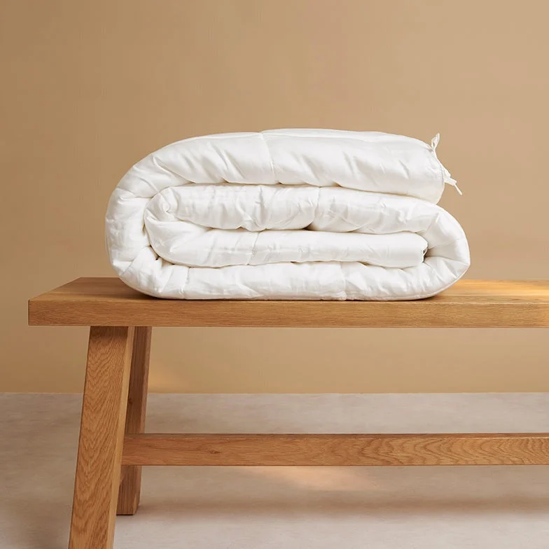 Het Dekbed 240x220 Oase van roest, netjes opgevouwen, rust op een houten bank tegen een beige achtergrond.