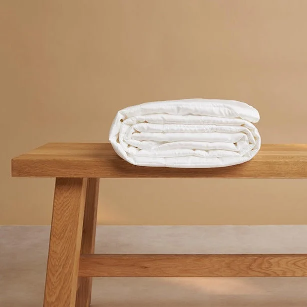 De Dekbed 240x220 Stijlvolle upgrade is netjes opgevouwen op een eenvoudige houten bank, tegen een effen beige achtergrond.