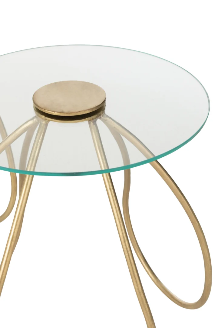 De Bijzettafel Goud Rond Metaal heeft een rond blad van helder glas en goudkleurige metalen poten die naar buiten buigen in een strak, gelust modern ontwerp en aansluiten op een centrale gouden schijf onder het oppervlak.