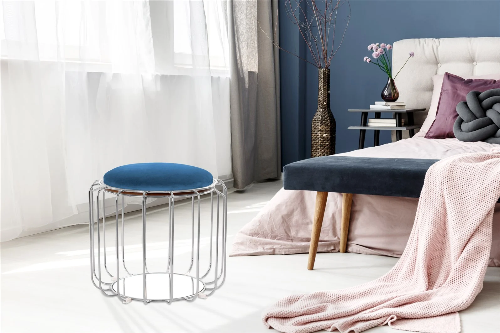 Moderne slaapkamer met een fluwelen bed, boeken, een decoratieve vaas en de Bijzettafel Zilver Mdf Design. Een metalen krukje met een blauw kussen en een roze deken op het bed; zonlicht schijnt door de transparante gordijnen.