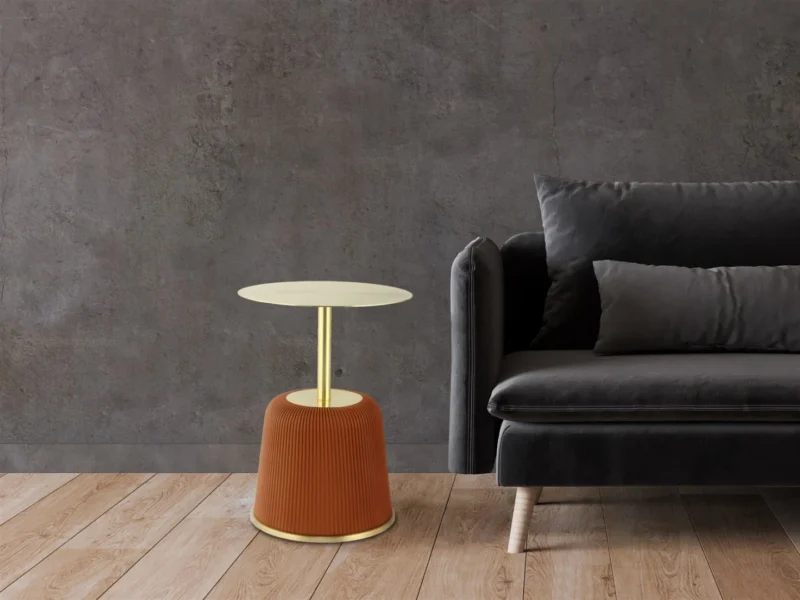 Een moderne woonkamer met een donkergrijze bank en twee kussens, naast de Bijzettafel 40 x 55 CM Rond Ijzer, die een gouden bovenkant en geribbeld oranje onderstel heeft, tegen een grijze muur met textuur en een houten vloer.