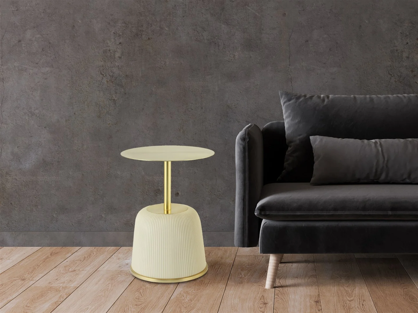 De Bijzettafel Crème Rond Ijzer, een klein modern rond bijzettafeltje met een gouden onderstel, staat naast een donkergrijze bank tegen een grijs gestructureerde muur op een houten vloer.