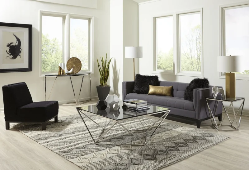 Moderne woonkamer met een grijze bank, zwarte stoel en de Aria gerookt glas en gepolijst roestvrijstalen bijzettafel. Een gedessineerd vloerkleed, staande lampen en grote ramen voegen natuurlijk licht en elegantie toe aan de neutraal getinte ruimte.