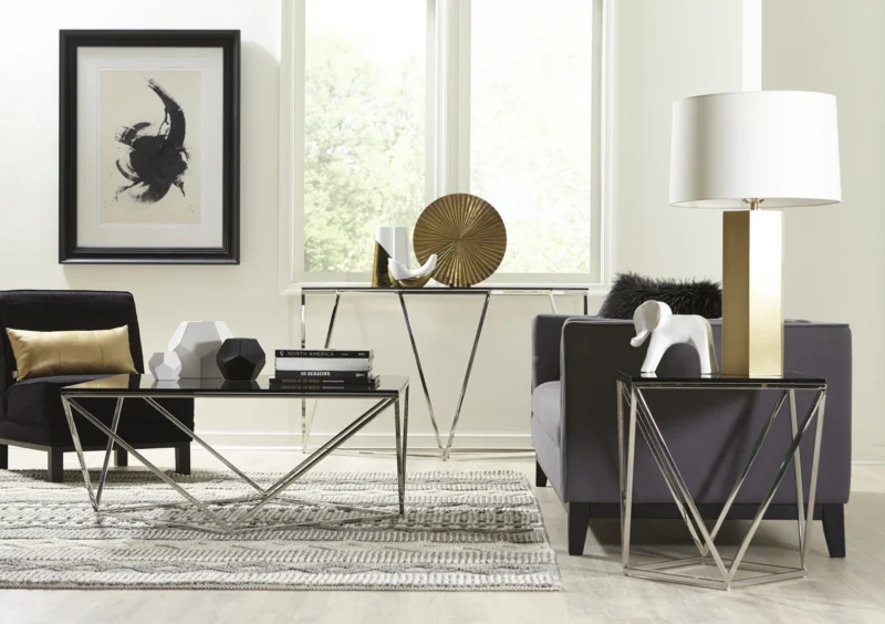 Moderne woonkamer met geometrische metalen meubels, zwarte fauteuils, decoratieve sculpturen, een tafellamp, abstracte muurkunst en de Aria gerookt glas en gepolijst roestvrijstalen bijzettafel. Grote ramen en een neutraal tapijt maken de ruimte compleet.