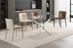 Een moderne eetkamer met de Tafel 'Lasi' 160 cm Glas met chromen poten, vier beige en bruine stoelen, een gestreept vloerkleed, een koffiezetapparaat op het aanrecht, decoratieve planken tegen een donkere muur en zonlicht uit een groot raam.