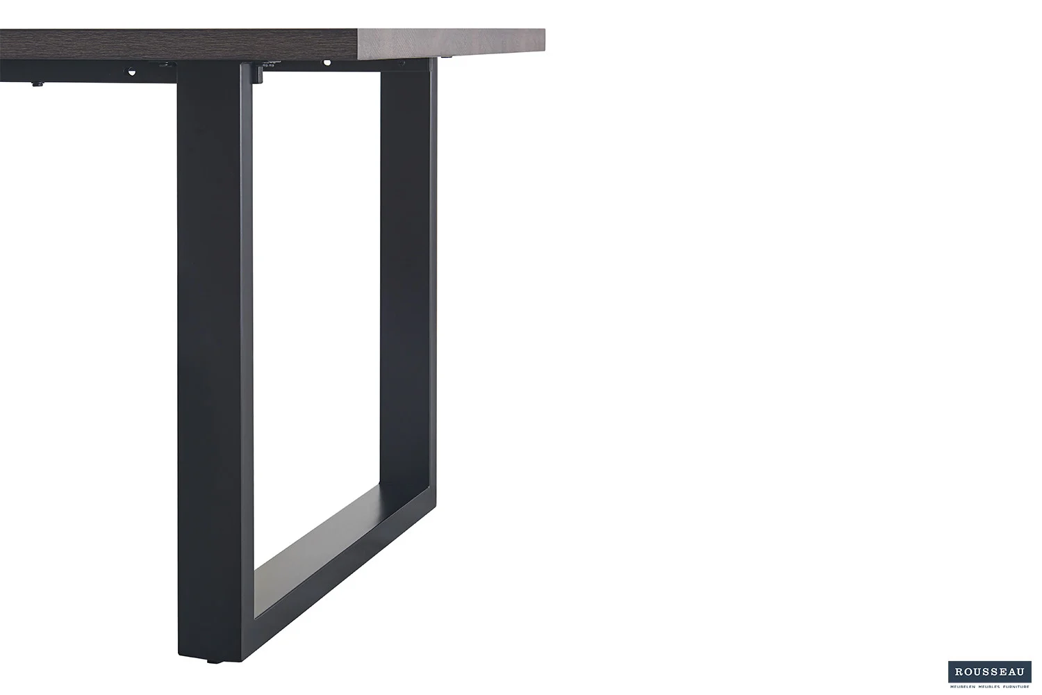 Een close-up van de UITVERKOOP - Tafel 'Alexander' 180 cm Decor Donkerbruin toont het donkere rechthoekige blad en de zwarte metalen geometrische poten tegen een witte achtergrond, met het logo van het merk Rousseau in de rechterbenedenhoek.