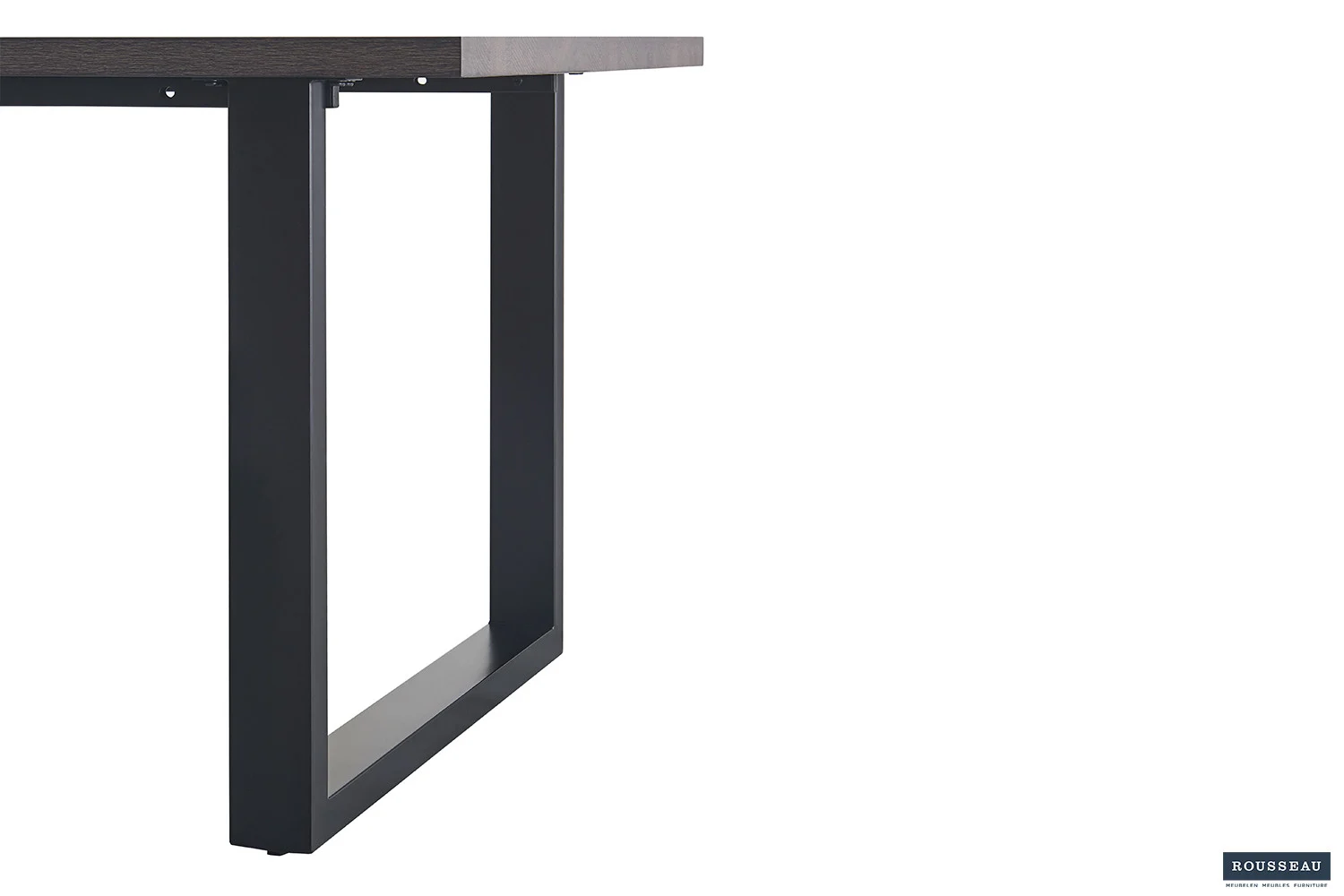 Close-up van de UITVERKOOP - Tafel 'Alexander' 200 cm Decor Donkerbruin, met een tafelblad met houtstructuur en donkere rechthoekige metalen poot op een witte achtergrond. Rousseau logo in rechter benedenhoek.