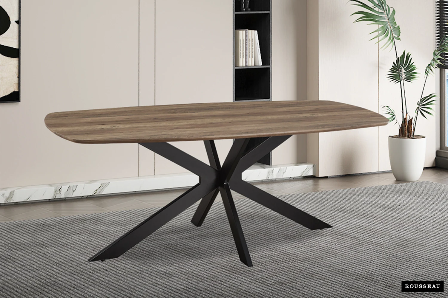 De Tafel 'Aziz' 200 cm Deens Ovaal Decor Mango heeft een eigentijds ontwerp met een mangohouten afwerking, staat op zwarte schuine poten en is geplaatst op een grijs vloerkleed in een moderne kamer met neutrale muren, een plant en een minimalistische inrichting.