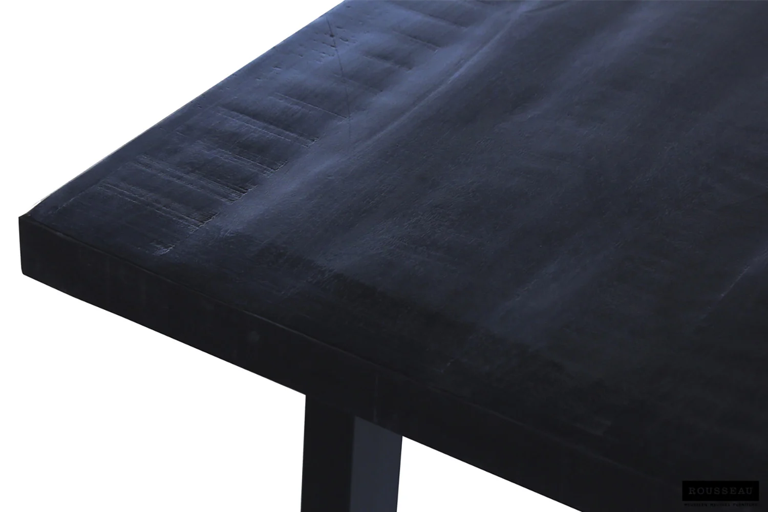 Een close-up van de hoek van UITVERKOOP - Tafel 'Nicola' 180 cm, een rechthoekige tafel van zwart mangohout met een gladde, matte afwerking en subtiele nerfpatronen, getoond tegen een witte achtergrond.