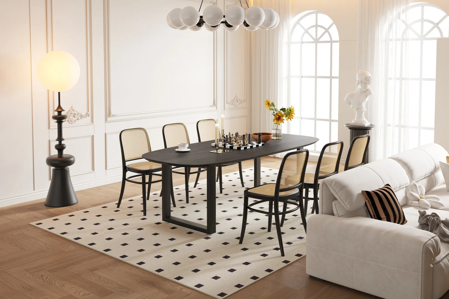 Een moderne eetkamer met de UITVERKOOP - Tafel 'Tommy' 220x100 cm Deens Ovaal U-Poot in zwart mangohout, zes stoelen met rieten rug, een schaakspel, witte bank, ronde staande lamp, grote boogramen, een beeld en gele bloemen.