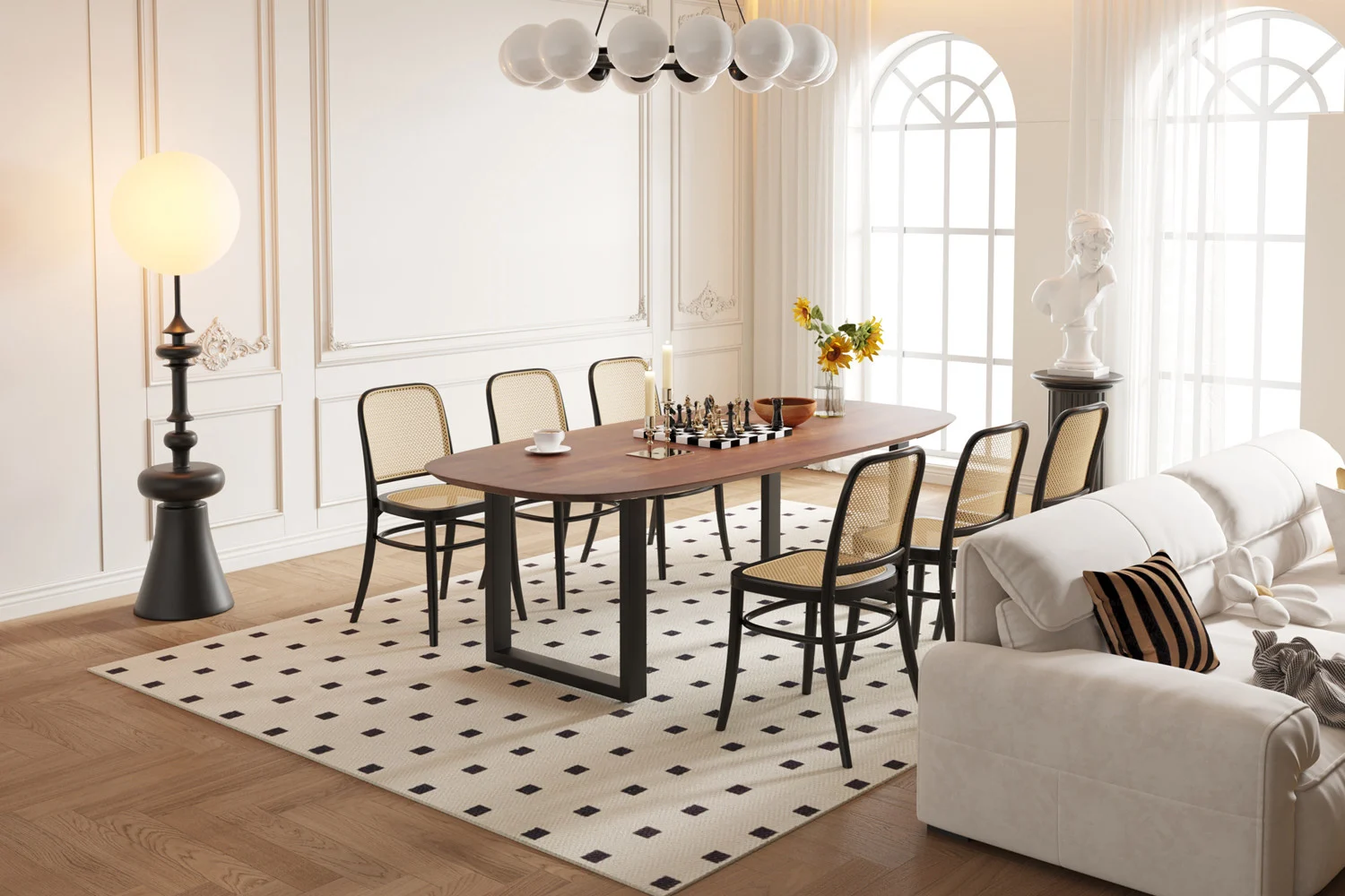 Een moderne eetkamer met de UITVERKOOP - Tafel 'Tommy' 220x100 cm Deens Ovaal U-Poot Mango hout Bruin, schaakset, zes stoelen met rieten rugleuning, een witte bank, vloerkleed met patroon, hoge ramen, staande lamp, buste sculptuur en vaas met bloemen.