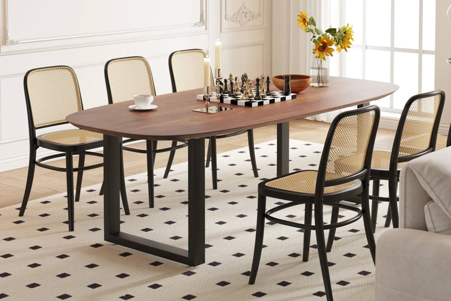 De 'UITVERKOOP - Tafel Tommy' 220x100 cm Deens Ovaal U-Poot Mango hout Bruin is afgebeeld met zes rieten stoelen op een gedessineerd kleed, met daarop een schaakspel, kop en schotel, kandelaars, schaal en zonnebloemen bij een zonovergoten raam.