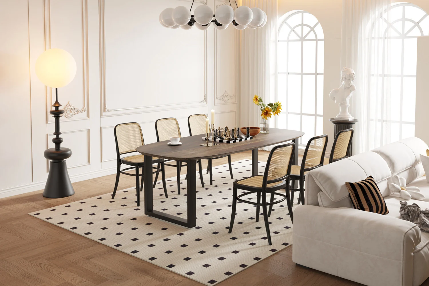 In een lichte, elegante eetkamer staat de UITVERKOOP - Tafel 'Tommy' 220x100 cm Deens Ovaal U-Poot Mango hout Tabaco tafel, gedekt voor schaken, met zes stoelen, een bank, zwarte lamp, grote ramen, bloemen, een beeld en een geometrisch vloerkleed op houten vloeren.