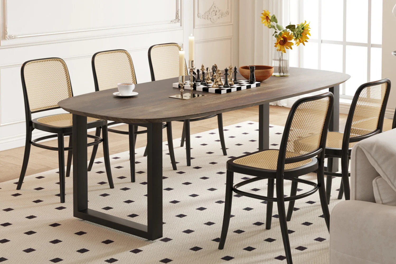 In een eetkamer staat de UITVERKOOP - Tafel 'Tommy' 220x100 cm Deens Ovaal U-Poot in Tabaco mangohout, omringd door zes stoelen met geweven rugleuning, een schaakbord, kaarsen, een beker, een schaal en zonnebloemen in een vaas bij een zonovergoten raam op een vloerkleed met patroon.