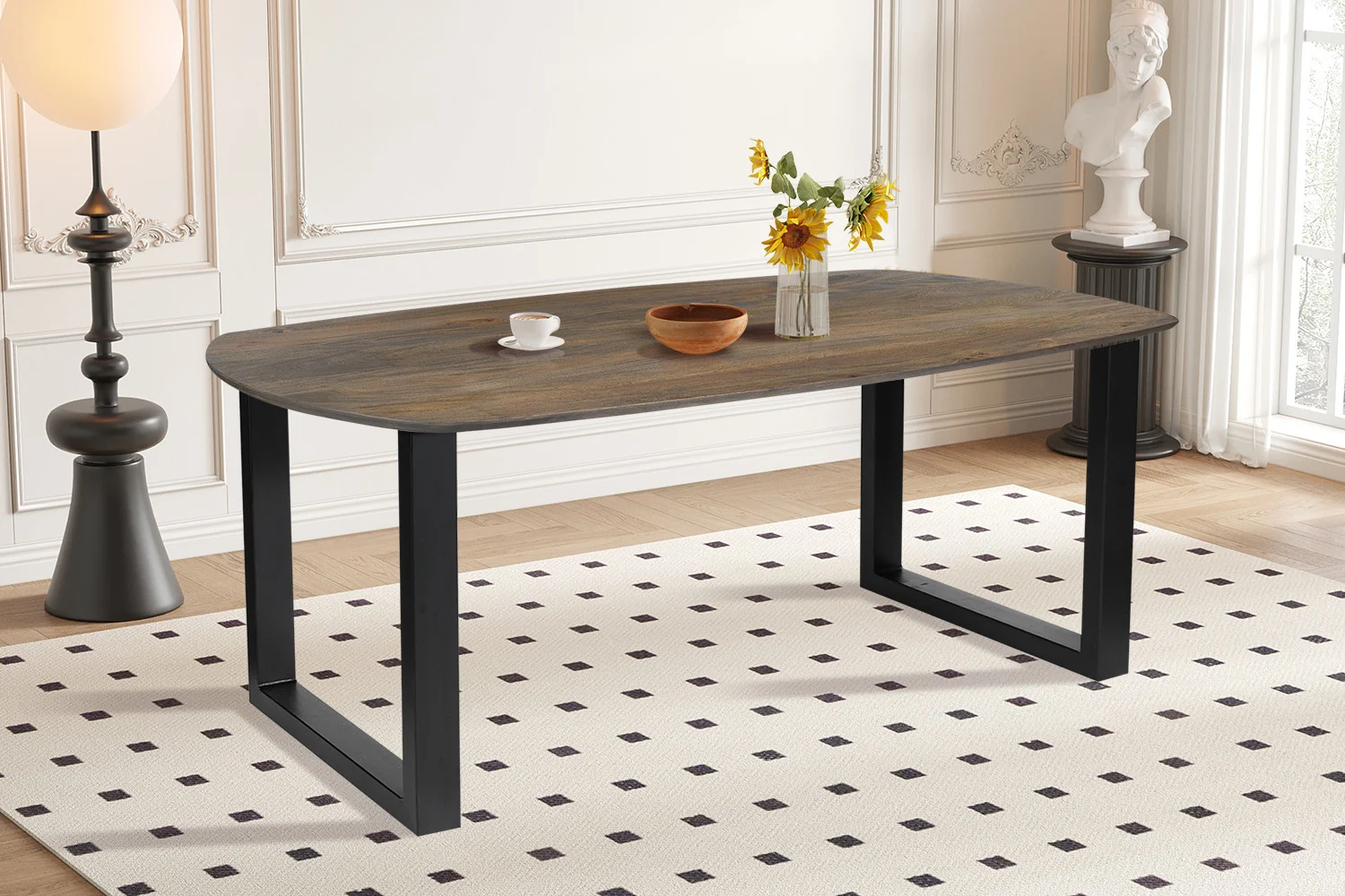 De UITVERKOOP - Tafel 'Tommy' 220x100 cm Deens Ovaal U-Poot van tabakskleurig mangohout staat op een wit kleed met zwarte vierkanten. Op de tafel staan een glazen vaas met zonnebloemen, een wit kopje met schotel en een houten schaal.