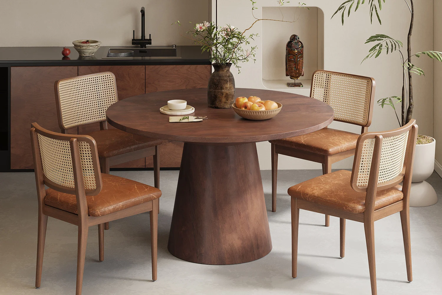 De Tafel 'Tommy' 130 cm rond in bruin mangohout is vormgegeven met vier stoelen met rieten rugleuning, een bloemenvaas en een fruitschaal, in een moderne keuken met minimalistische inrichting en potplanten.