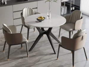 Een moderne eethoek met de Tafel 'Apollo' 110 cm Rond Glanzend Steen Sneeuwwit, vier beige gecapitonneerde stoelen, een fruitschaal en een glazen vaas op een grijs marmeren vloer met strakke kasten op de achtergrond.