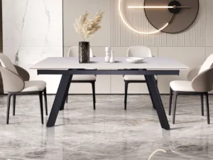 In een moderne eetkamer staan de Uitschuifbare tafel 'Hera' 160-240 cm Rechthoekig Steen Wit, vier stoelen met kussens, een vaas met gedroogd pampagras, twee kandelaars en een wandklok op marmeren vloeren met decoratieve wandpanelen.