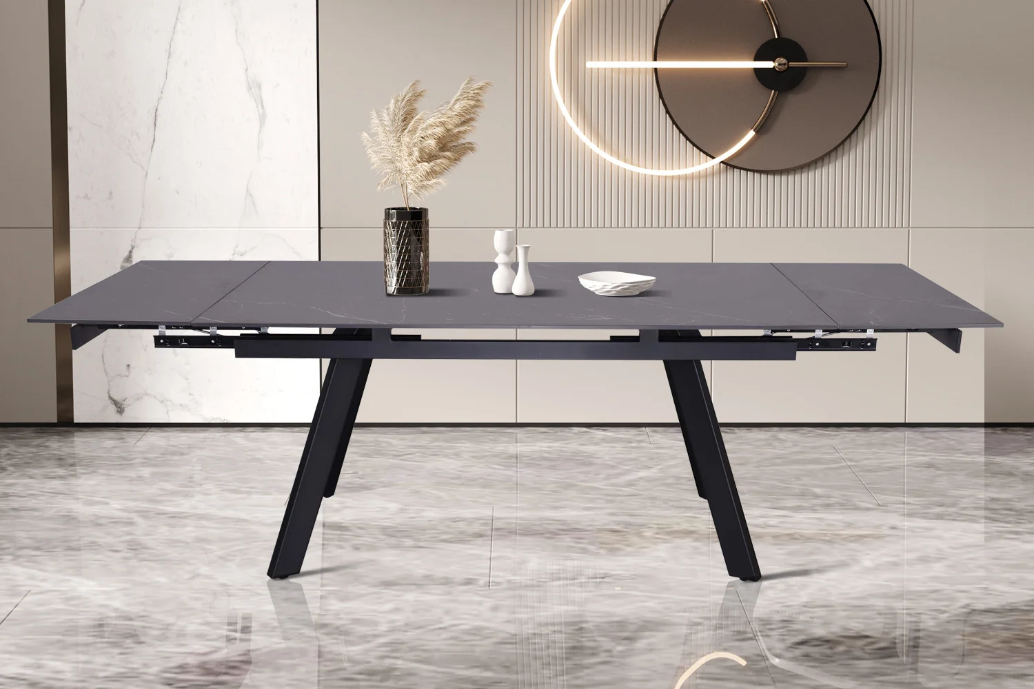 De Uitschuifbare tafel 'Hera' 160-240 cm Rechthoekig Steen Zwart staat op een spiegelende marmeren vloer, met daarop een vaas met pampagras, twee peper- en zoutvaatjes en een klein bordje. Op de achtergrond hangt een wandklok.