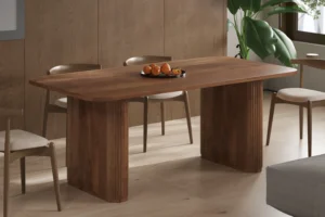 De Tafel 'Jean' 200 cm Deens Ovaal in lichtbruin mangohout staat in het midden, gekoppeld aan vier houten stoelen met kussens. Op tafel staat een bord sinaasappels; op de achtergrond zorgt een grote groene plant voor extra frisheid.