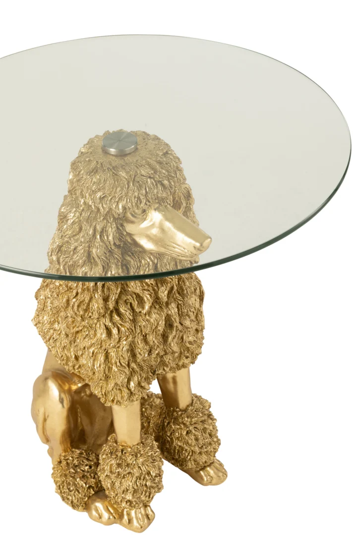 De Bijzettafel Poedel Rond Polyresin Goudkleurig is een ronde tafel van glas met een goudkleurige poedelbasis van polyresin, met het lichaam en de kop van de hond als ondersteuning.