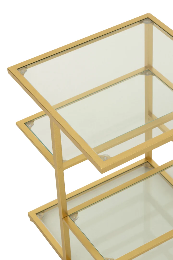 Een close-up van de Bijzettafel ijzer/glas goudkleurig toont het moderne goudkleurige metalen frame en de drie glazen legplanken, die een geometrisch ontwerp met transparante oppervlakken hebben.