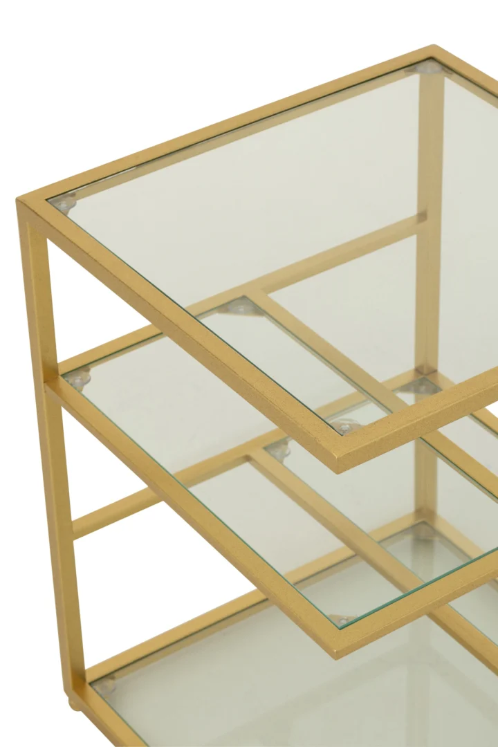 Een close-up van de Bijzettafel ijzer/glas goudkleurig, een moderne bijzettafel met een frame van goudkleurig metaal, planken van helder glas en een geometrisch ontwerp met meerdere niveaus.