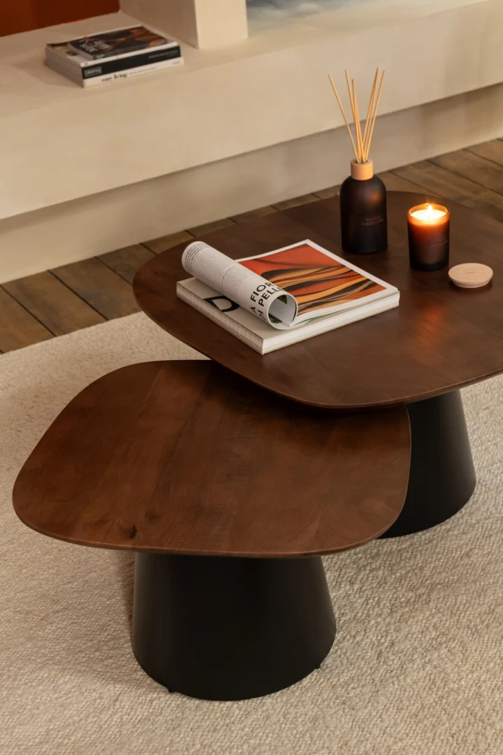 De Bijzettafel Zwart, Bruin 74 x 43 CM, een moderne vierkante salontafel van mangohout met overlappende bladen, toont een tijdschrift, boek, geurkaars en rietverspreider op een licht getextureerd tapijt.