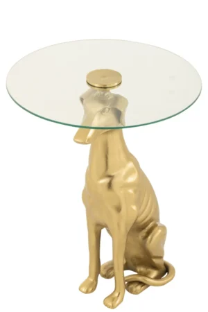 De Bijzettafel Transparant 46 x 58 CM is een ronde bijzettafel met een transparant glazen blad en een aluminium onderstel in de vorm van een goudkleurige zittende hond, die lijkt op een windhond.