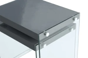Een close-up van de Bijzettafel Zwart Glas Compact, met een glanzend donkergrijs glazen blad en helder glazen zijkanten verbonden door metalen bouten.