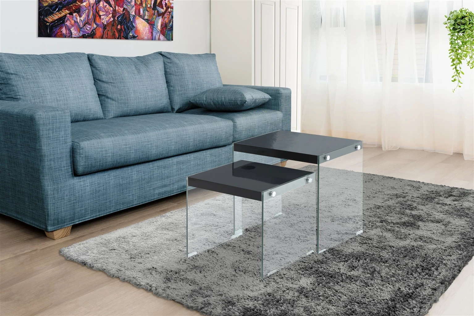 Een moderne woonkamer met een blauwe bank, een grijs vloerkleed, twee Bijzettafel Zwart Glas Compact tafels, een kleurrijke muurschildering en transparante witte gordijnen die natuurlijk licht binnenlaten.