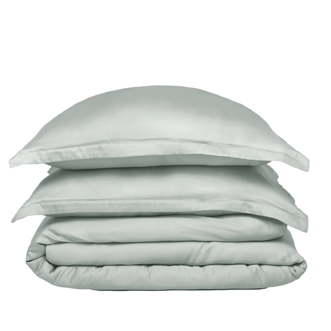 De Dekbedovertrek 140x220 Luxe uitstraling is netjes opgevouwen in lichtgrijs, gestapeld met twee bijpassende kussenslopen en een kussen tegen een effen witte achtergrond.