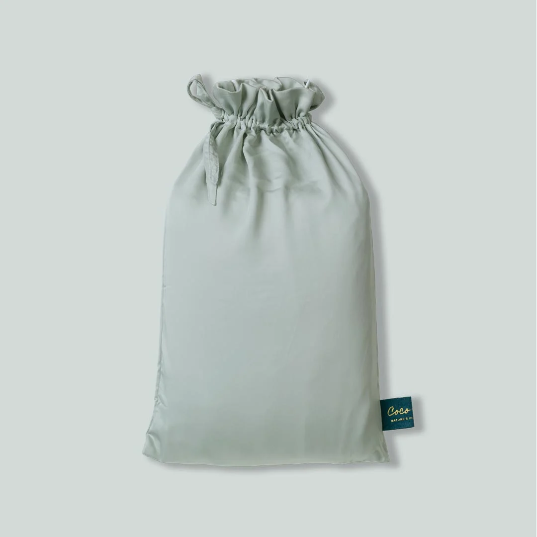 Zachte, lichtgroene Tencel hoeslaken verpakt in een satijnen zak met trekkoord. Zachte belichting, minimalistische stijl.