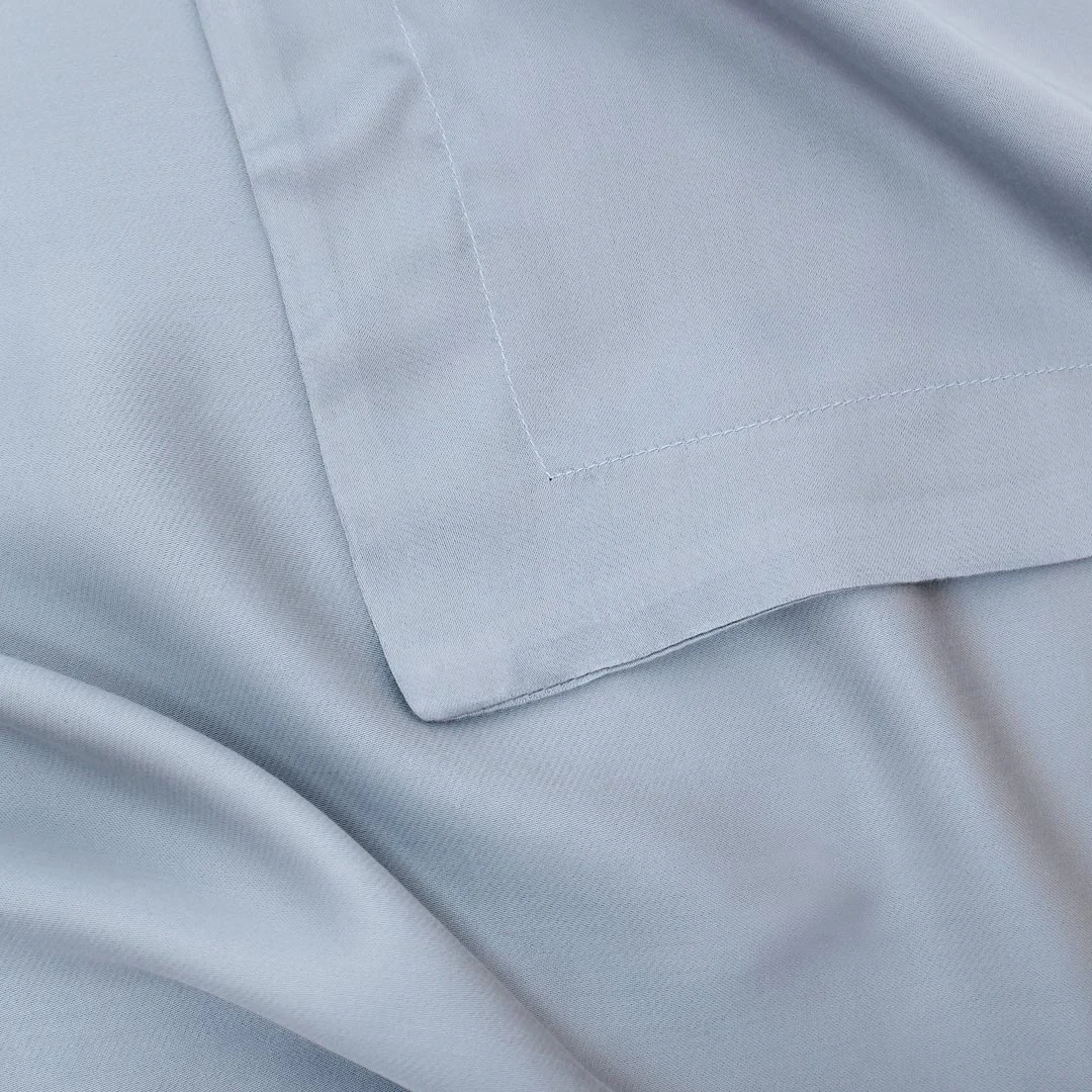 Close-up van de Dekbedovertrek 200x200 Diervriendelijke keuze in lichtgrijs of lichtblauw, met de nadruk op de gladde textuur, zachte drapering en netjes gestikte gevouwen rand.
