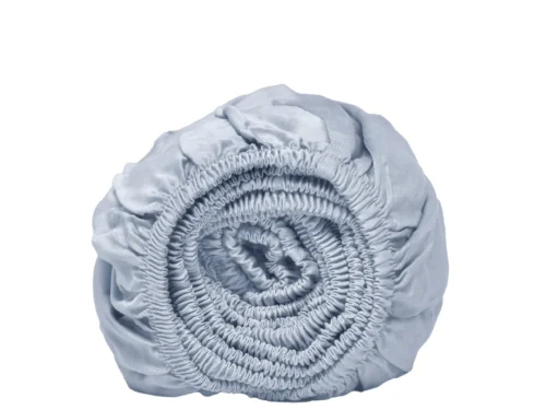 Oprolbaar, lichtblauw hoeslaken van Tencel, close-up. Zachte stof met elastische rand op een witte achtergrond. Ademend en koel materiaal.