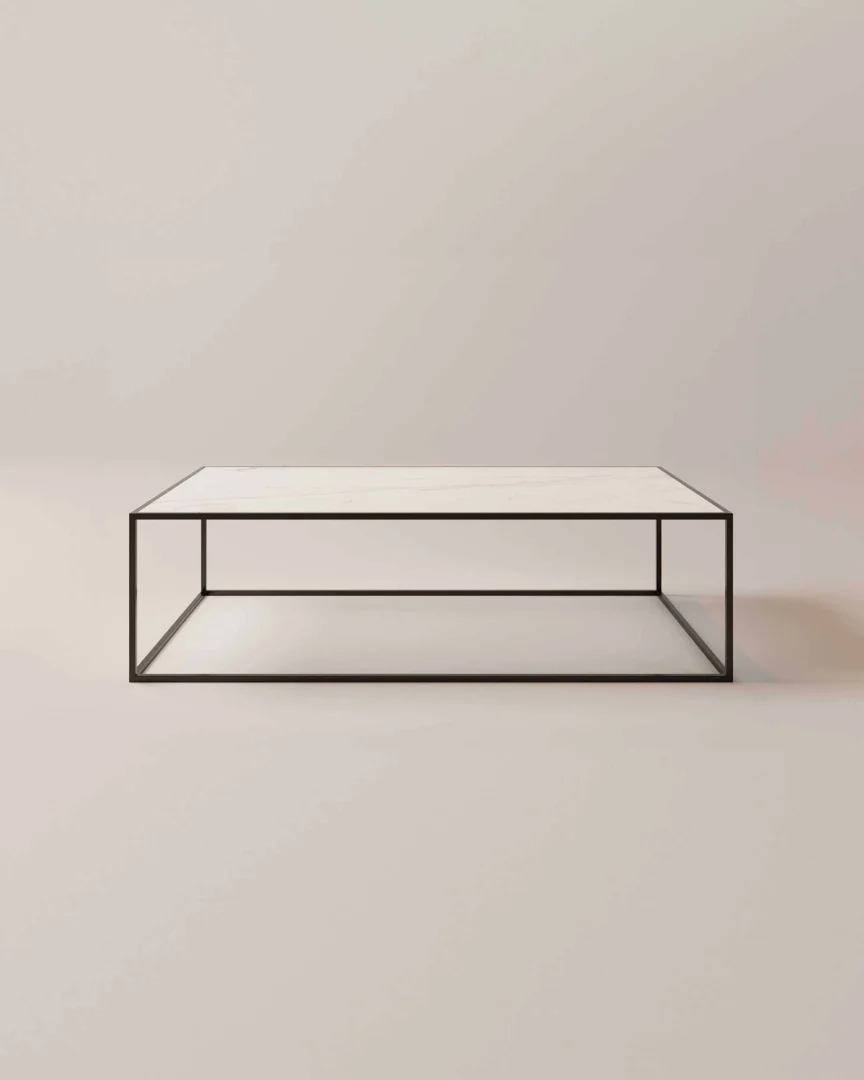 De Salontafel Zwart heeft een tijdloos industrieel en klassiek ontwerp, met een minimalistisch zwart metalen frame en een rechthoekig wit blad, afgebeeld tegen een lichte achtergrond.