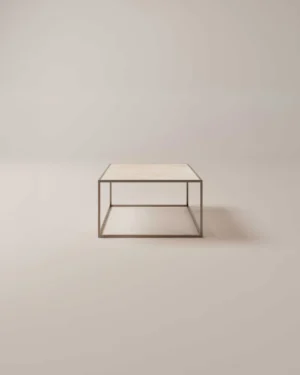 De Salontafel Brons Rond is een minimalistische ronde salontafel met een dun metalen frame en een lichtgekleurd tafelblad tegen een effen, neutrale achtergrond.