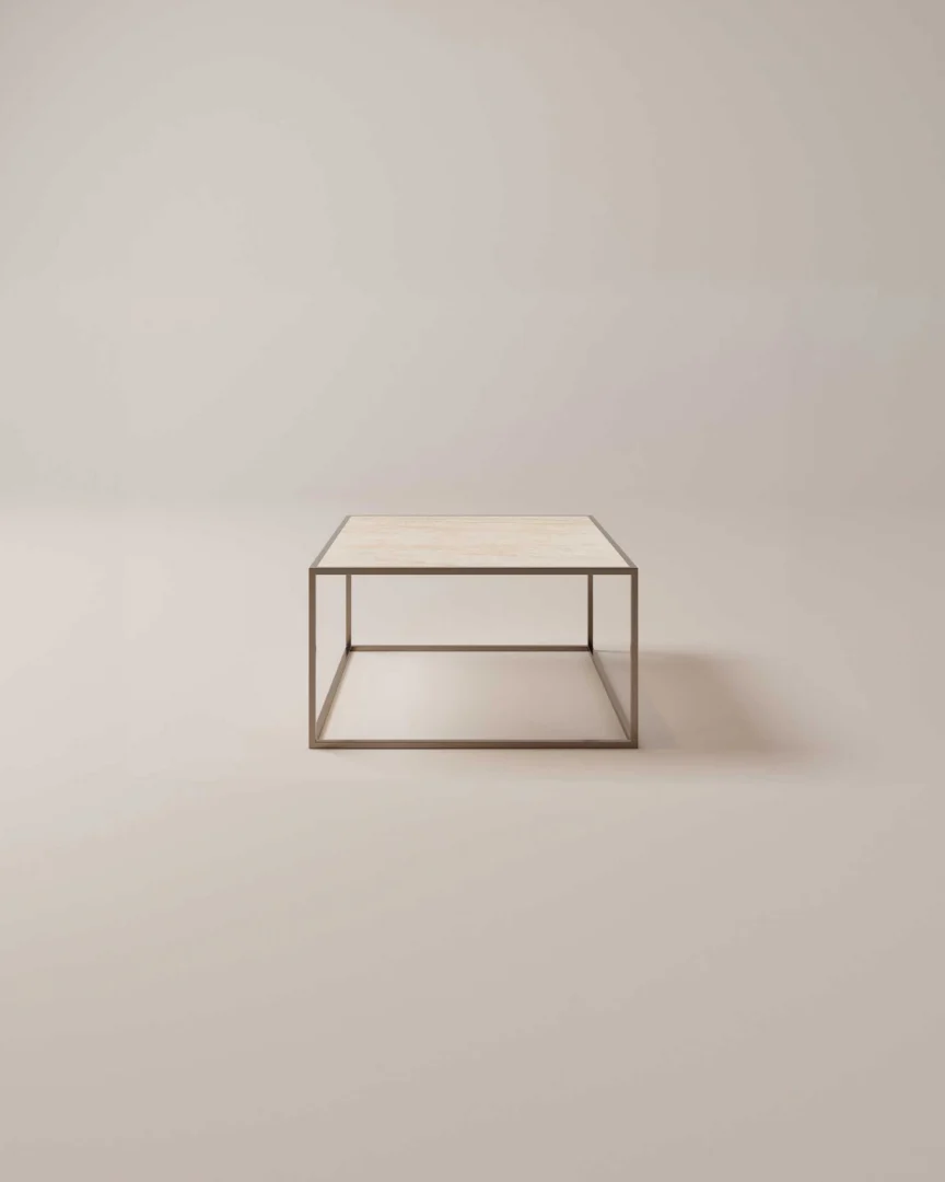 De Salontafel Brons Rond is een minimalistische ronde salontafel met een dun metalen frame en een lichtgekleurd tafelblad tegen een effen, neutrale achtergrond.