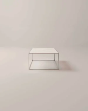 De Salontafel Zilver Keramiek is een minimalistische vierkante salontafel met een wit keramisch blad en een slank metalen frame, tegen een lichte achtergrond.