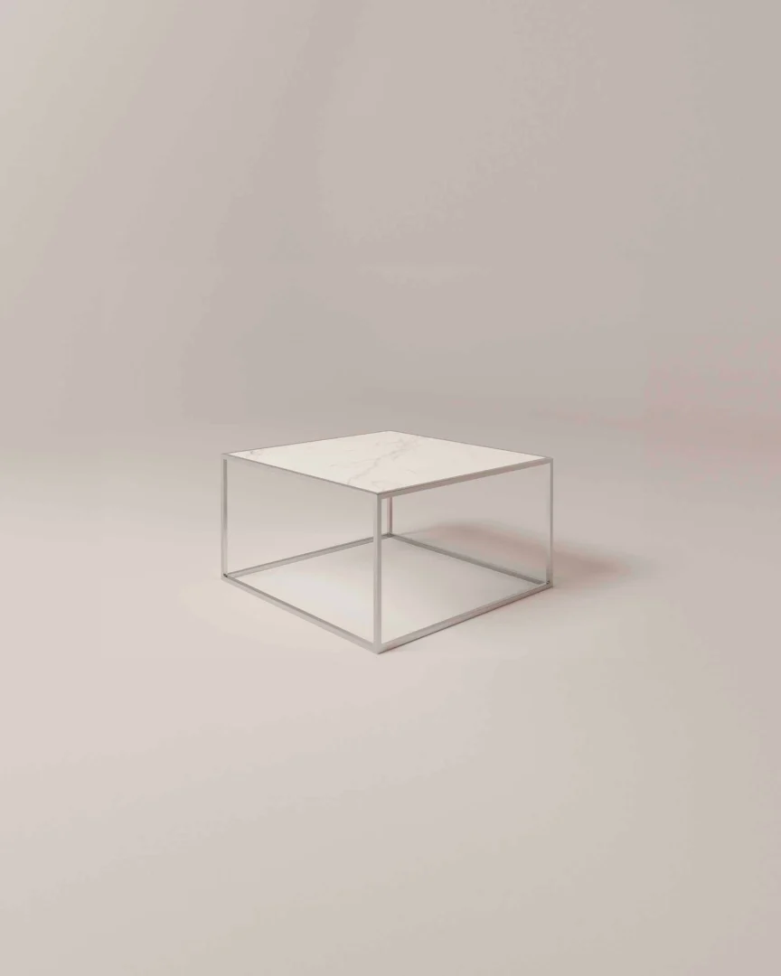 De Salontafel Zilver Keramiek is een minimalistische vierkante salontafel met een dun metalen frame en een wit marmeren blad tegen een effen, lichtgekleurde achtergrond.