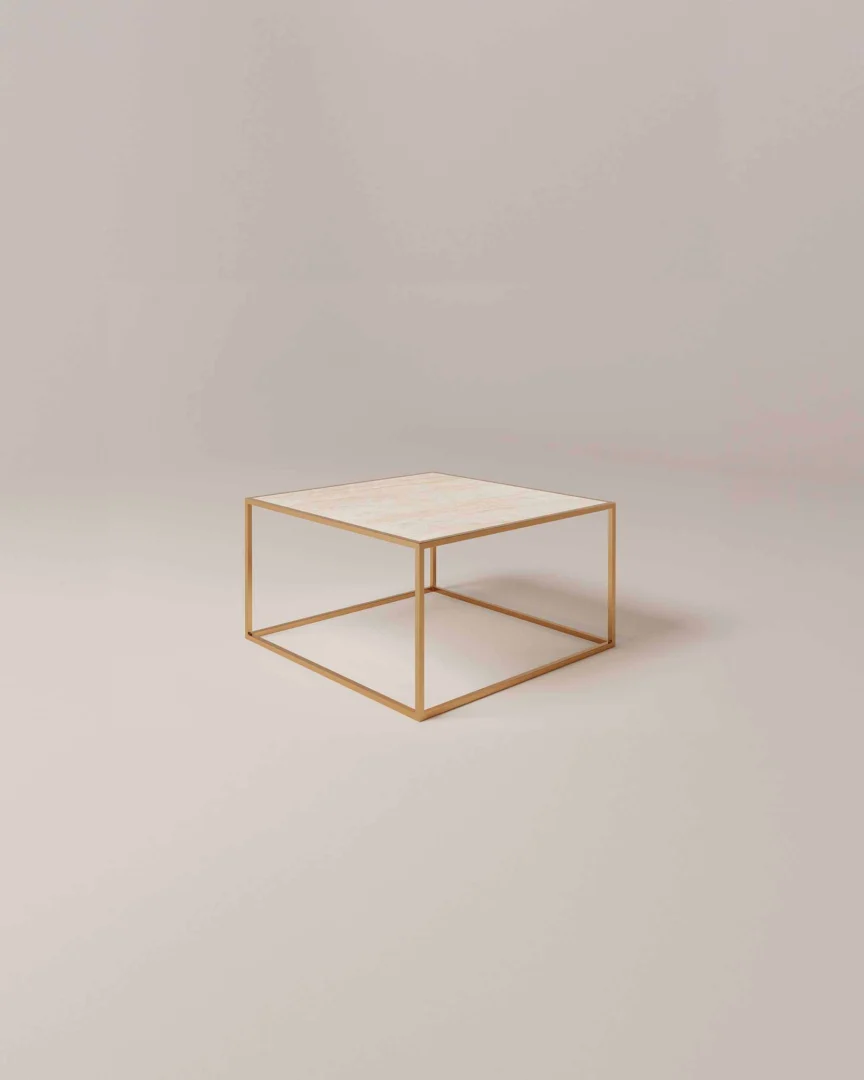 De Salontafel Messing Design is een minimalistische vierkante salontafel met een dun goud metalen frame en een licht marmeren blad tegen een effen beige achtergrond.