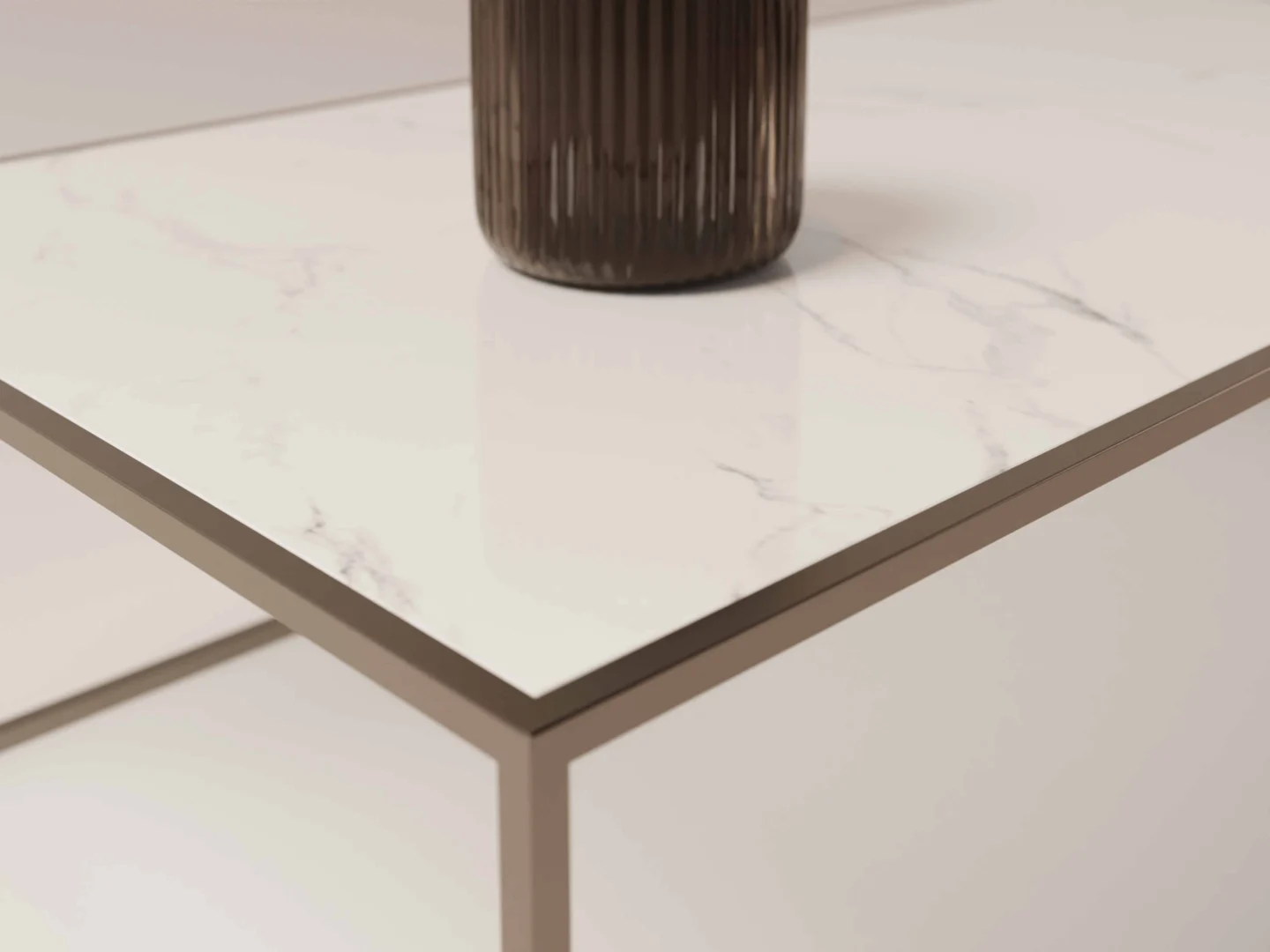 Close-up van de Salontafel Brons Chique, met een wit marmeren blad en metalen onderstel. Een geribbelde, donkere cilindervormige vaas is gedeeltelijk zichtbaar op de heldere, moderne tafel.