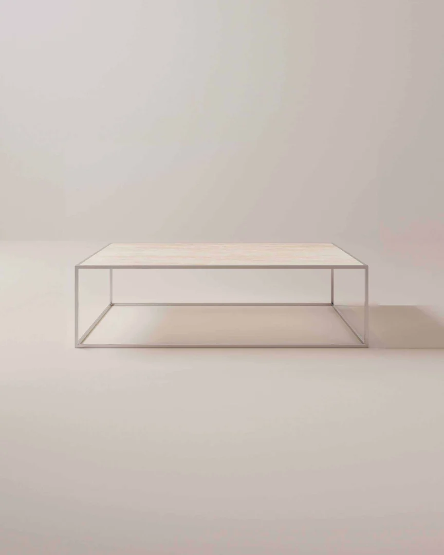 De Salontafel Zilver Klassiek, met een licht houten blad en een open rechthoekig metalen frame, staat elegant in een zacht verlichte, neutrale ruimte.