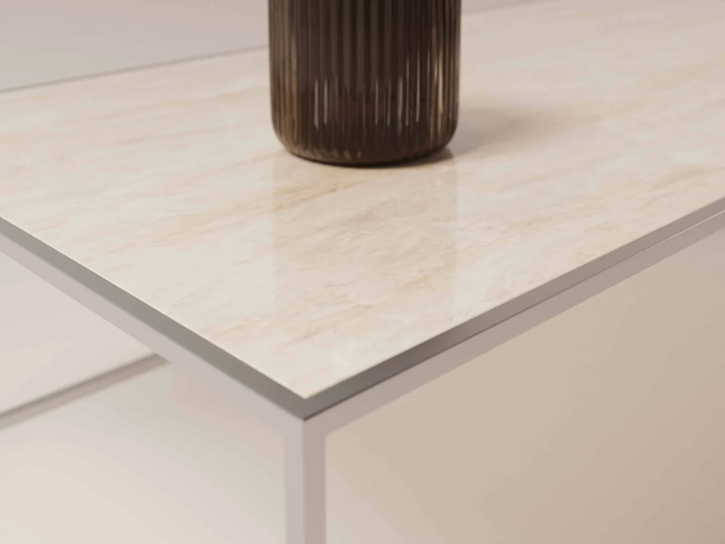 Een close-up van de Salontafel Zilver Klassiek toont het lichtgekleurde, glanzende marmeren blad en het witte metalen onderstel. De basis van een donkere, geribbelde vaas is gedeeltelijk zichtbaar op het glanzende tafelblad.