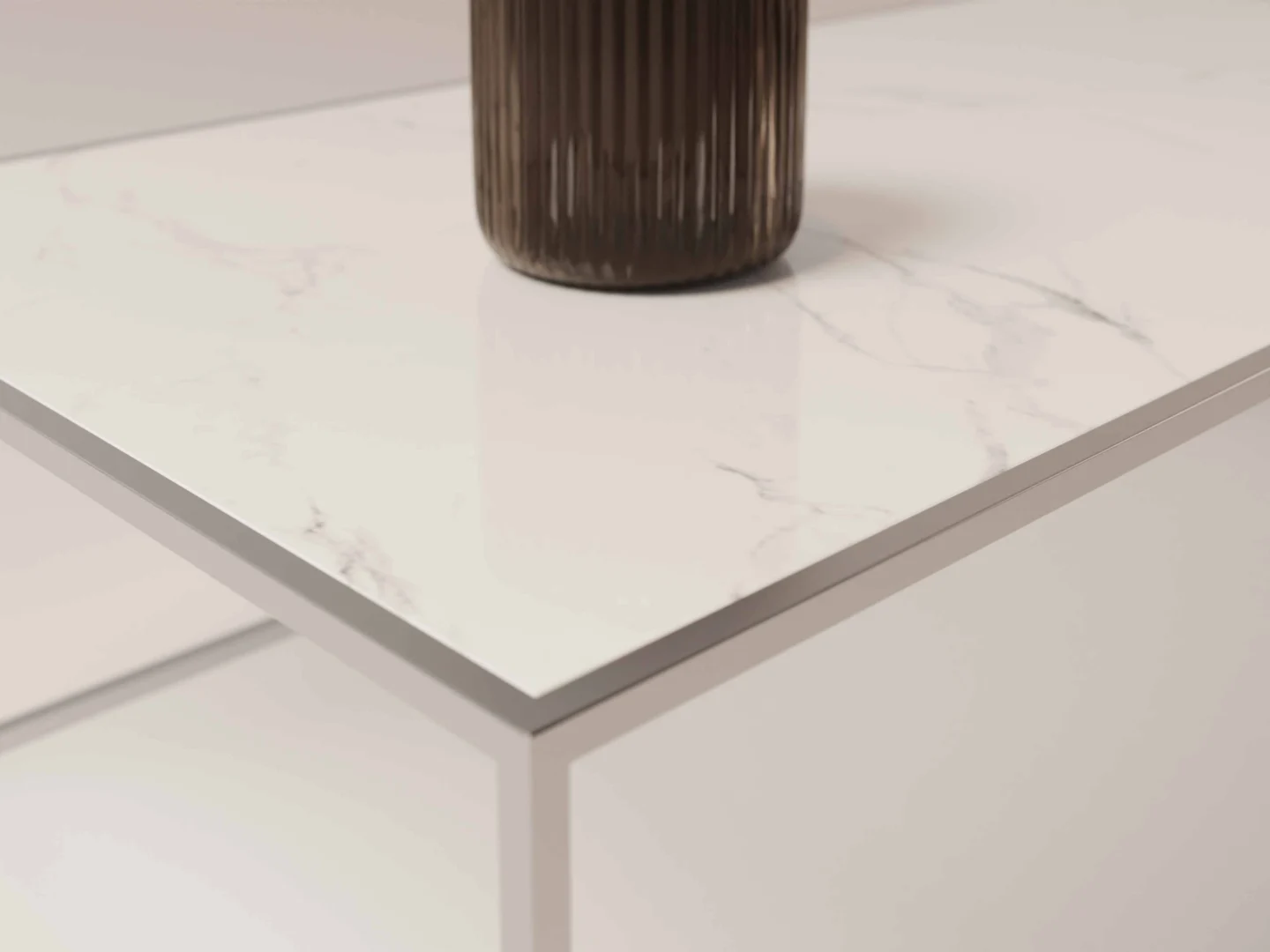 Een close-up van de Salontafel Zilver van Roest Design toont het wit marmeren blad met metalen randen. Een geribbelde, donkerbruine cilindrische vaas rust op het moderne oppervlak, tegen een minimale en vage achtergrond.