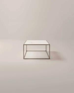 De Salontafel Brons Compact is een minimalistische vierkante salontafel met een dun metalen frame en een wit marmeren blad, afgebeeld tegen een effen, lichtgekleurde achtergrond.
