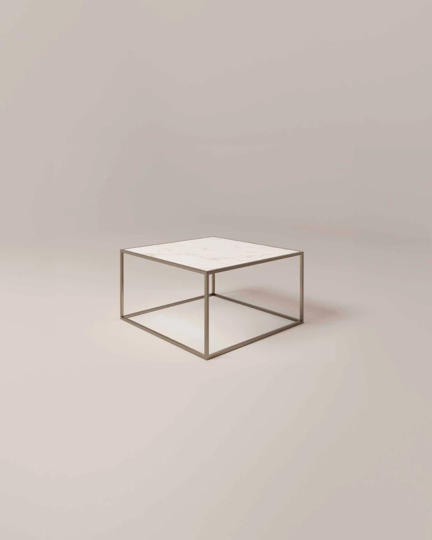 De Salontafel Brons Compact is een minimalistische vierkante salontafel met een dun metalen frame en een wit marmeren blad tegen een effen, neutrale achtergrond.