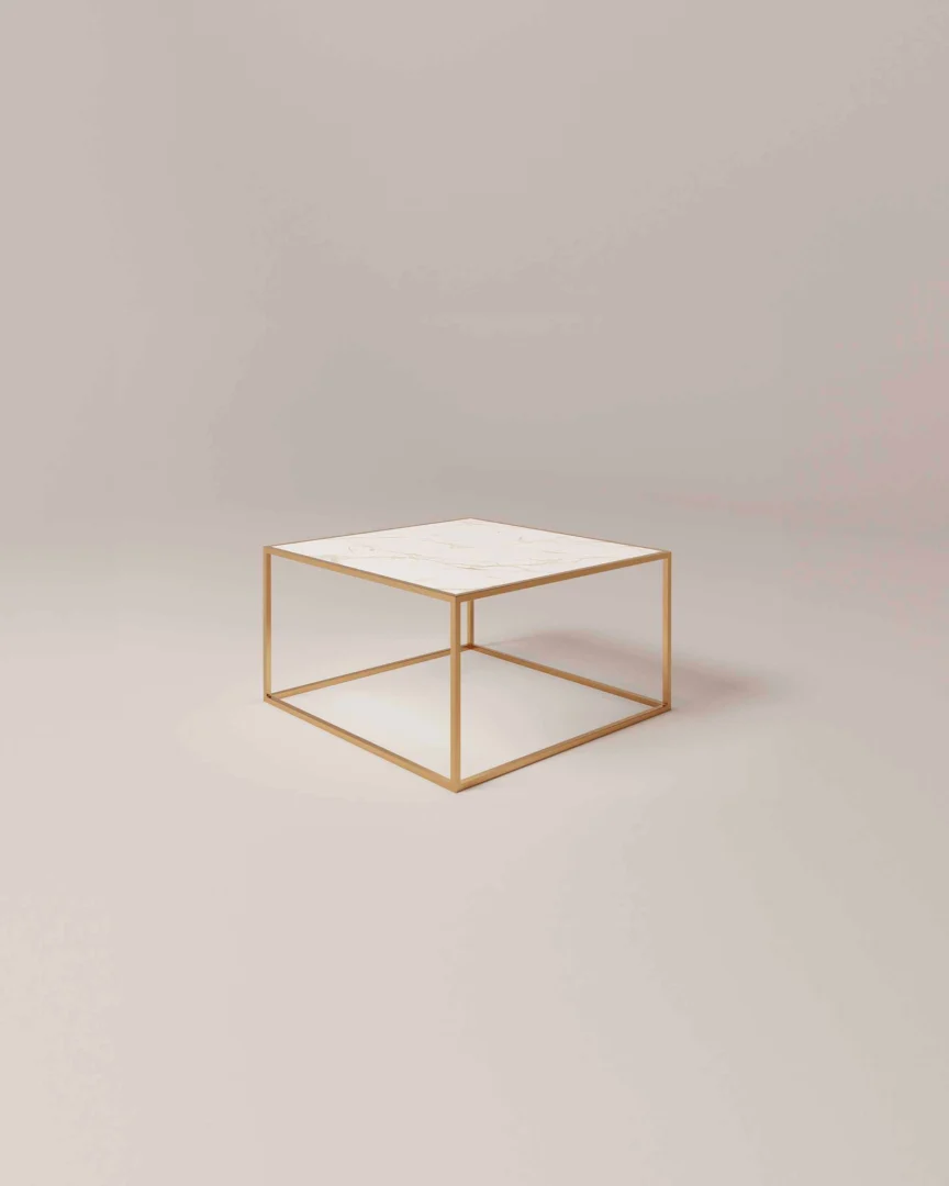 De Salontafel Messing Klassiek is een minimalistische vierkante salontafel met een dun, goudkleurig metalen frame en een wit marmeren blad tegen een effen, lichtgekleurde achtergrond.